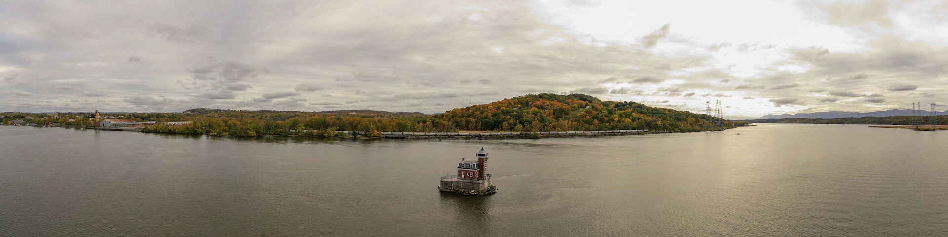A calm river with a small island covered in autumn foliage and a lighthouse in the center.