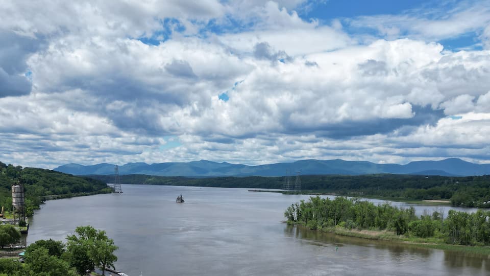A river with a bridge, a boat, and mountains in the background.