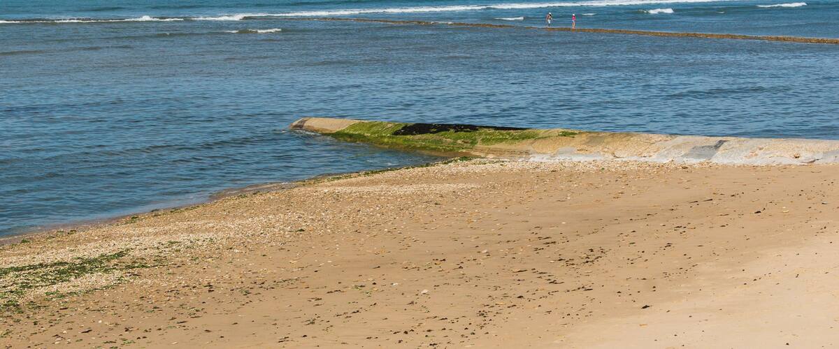 A sandy beach with calm sea and sailboats in the distance.