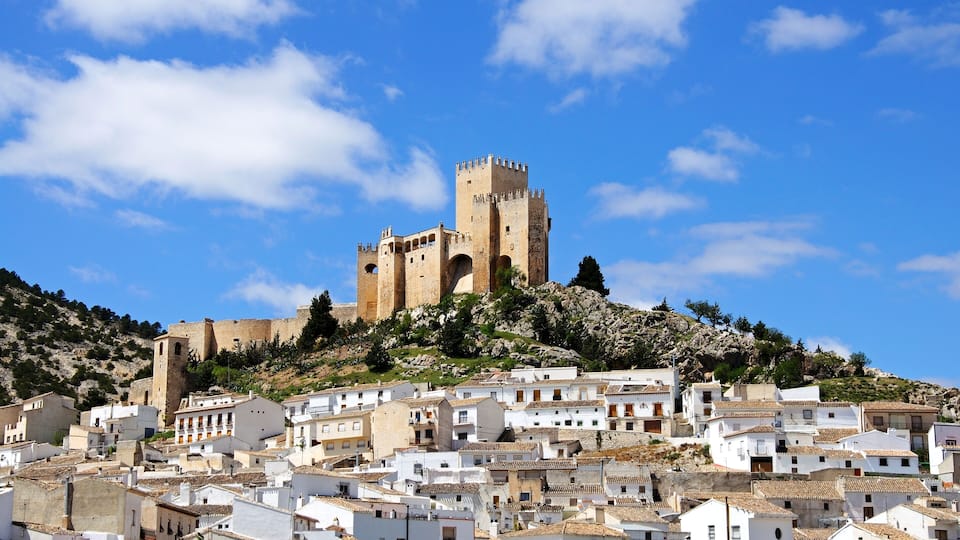 A historic town with white buildings and a prominent castle on a hill.