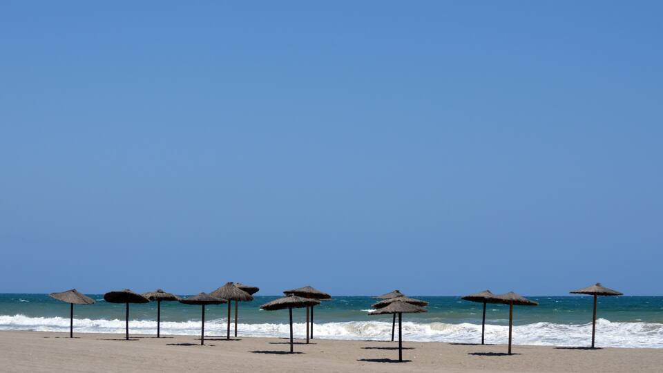 A beach with thatched umbrellas and the ocean in the background.