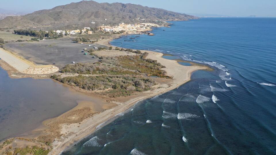 An aerial view of a coastal area with a beach, clear blue sea, and a town in the background.