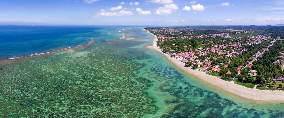 An aerial view of a coastal town with a beach, clear waters, and dense vegetation.