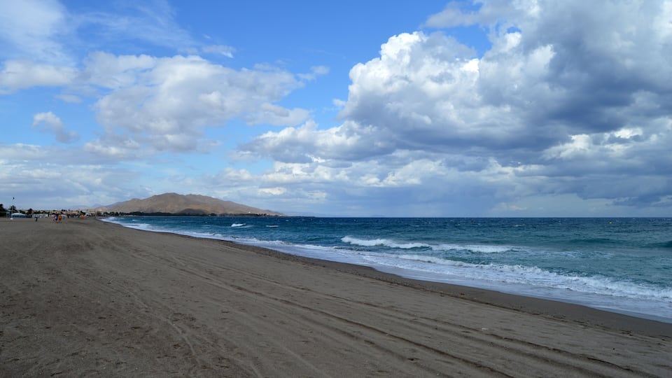 A beach with a mountain in the background and a partly cloudy sky.