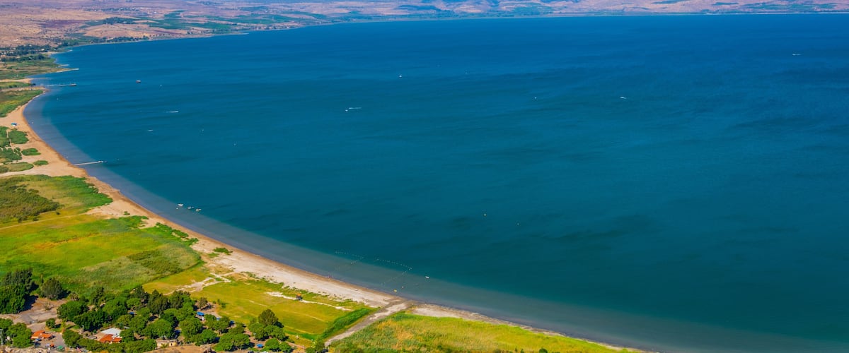 A coastal landscape with a wide beach, clear blue water, and distant mountains.