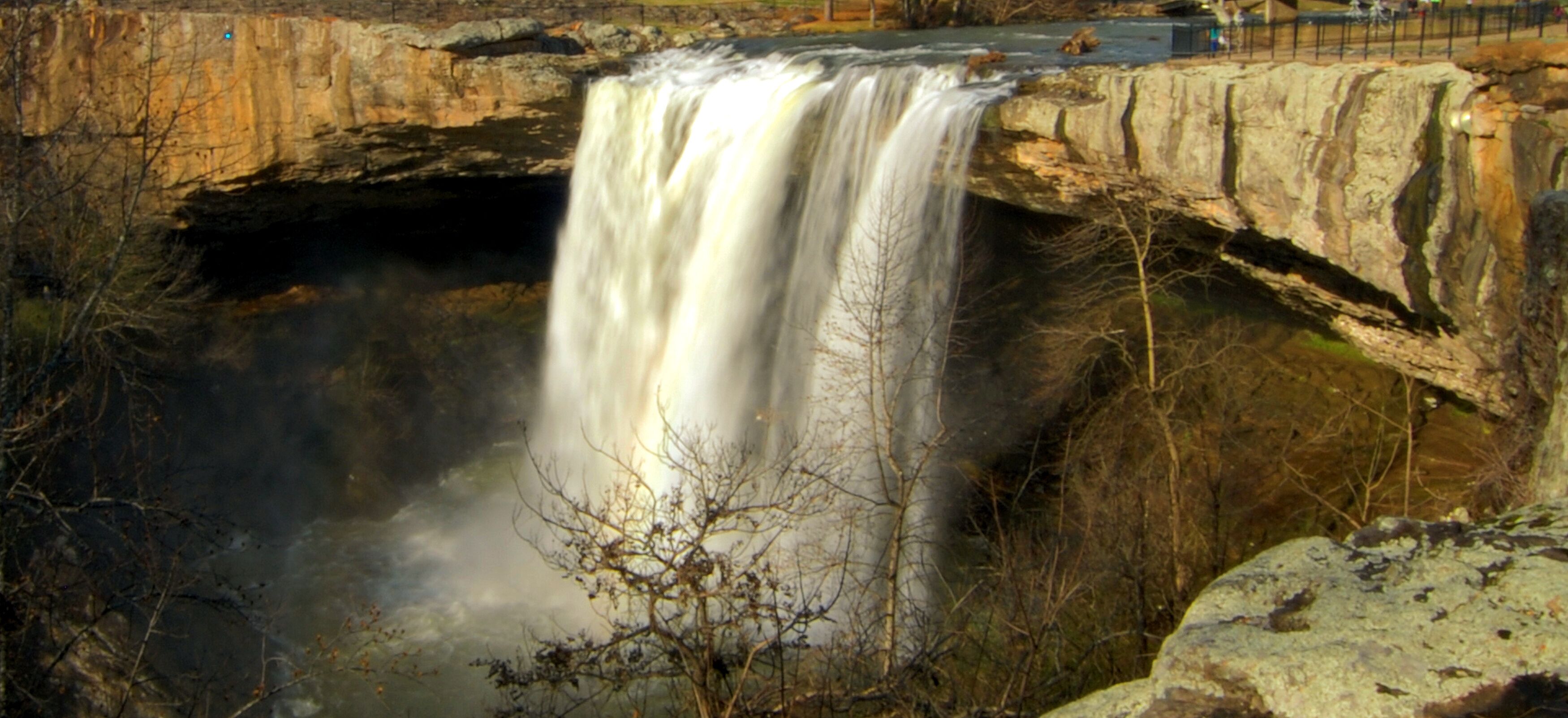A waterfall cascading over a rocky ledge with a bridge above.