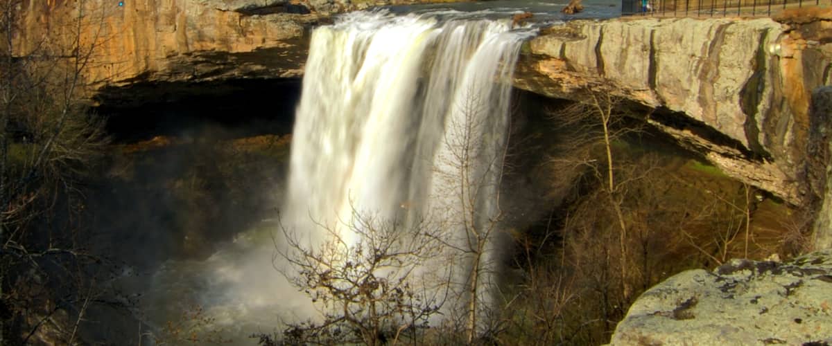 A waterfall cascading over a rocky ledge with a bridge above.