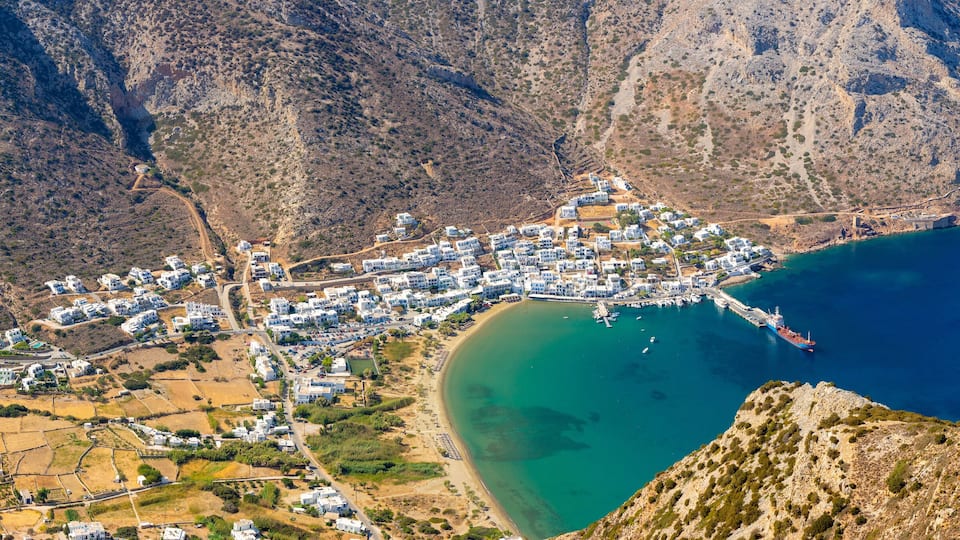 A coastal town nestled between mountains, with a clear blue sea and a winding road leading to the beach.