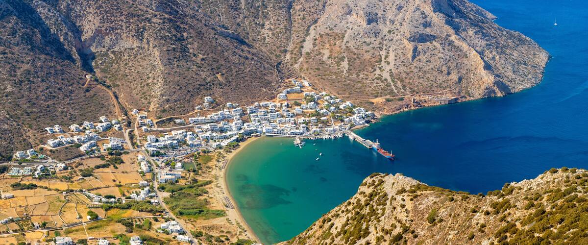 A coastal town nestled between mountains, with a clear blue sea and a winding road leading to the beach.