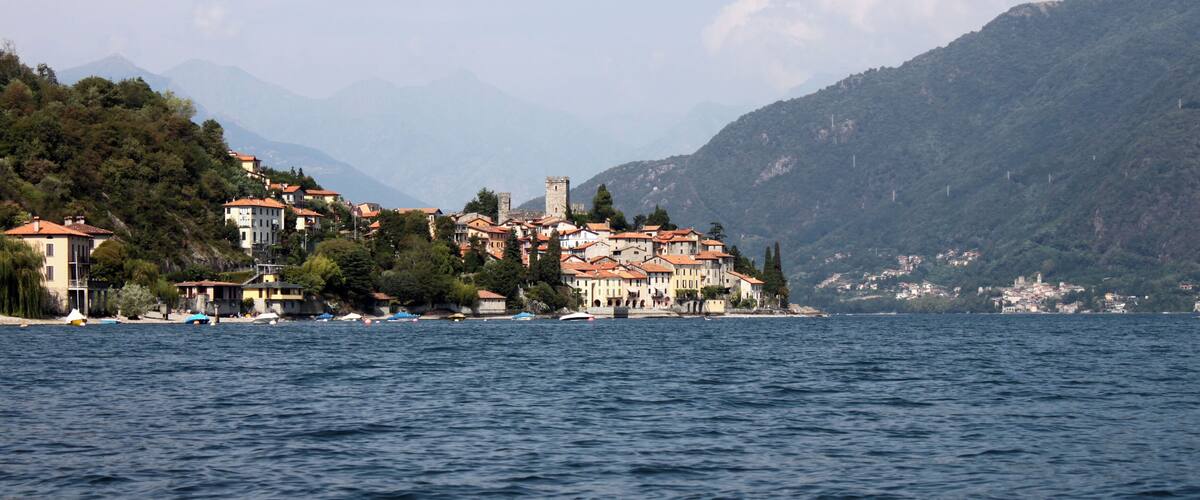 A lakeside village with buildings on a hillside, surrounded by mountains.