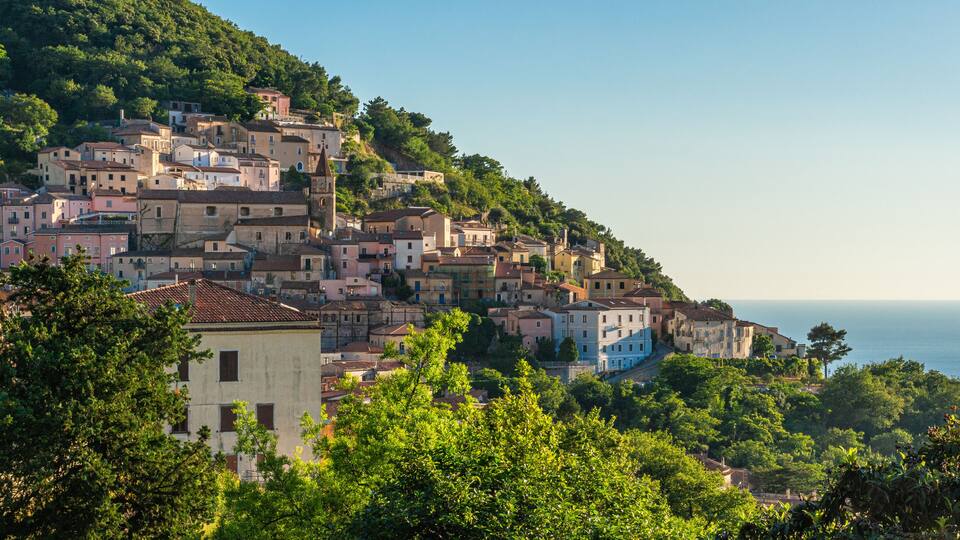 A coastal town with buildings on a hillside, a church, and the sea in the background.