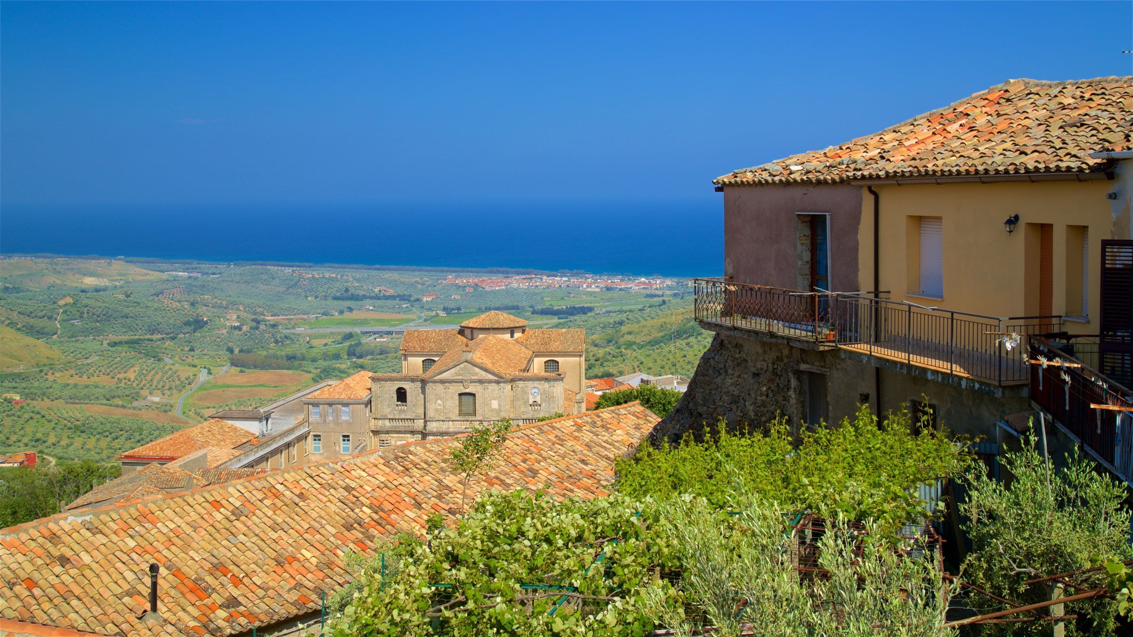 A coastal village with terracotta-roofed buildings, a stone church, and a view of the sea.