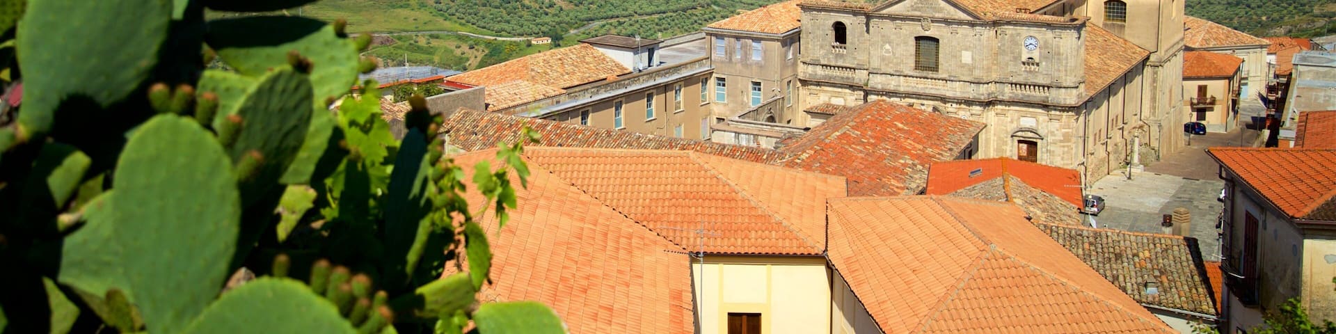 A coastal town with terracotta-roofed buildings, a prominent church, and a view of the sea and distant hills.