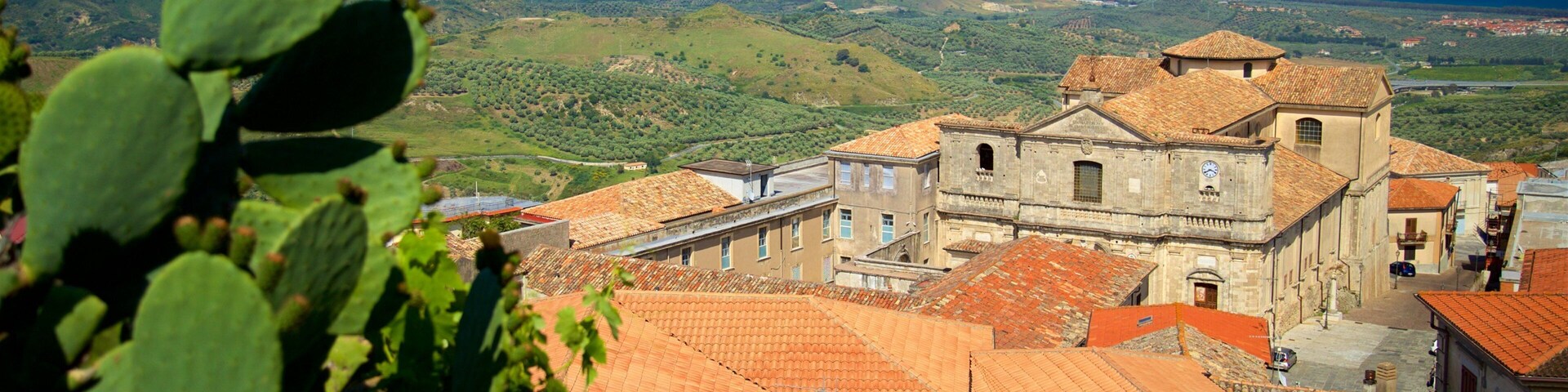 Un pueblo costero con edificios de tejas rojas, una iglesia destacada y vistas al mar y colinas lejanas.