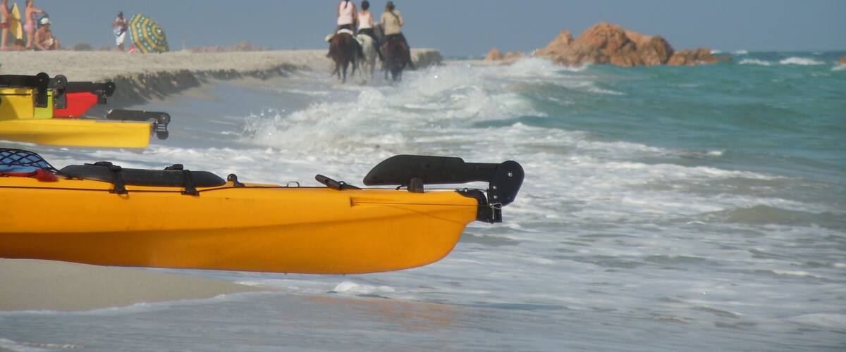 A beach with yellow kayaks, people in the water, and a rocky outcrop in the distance.