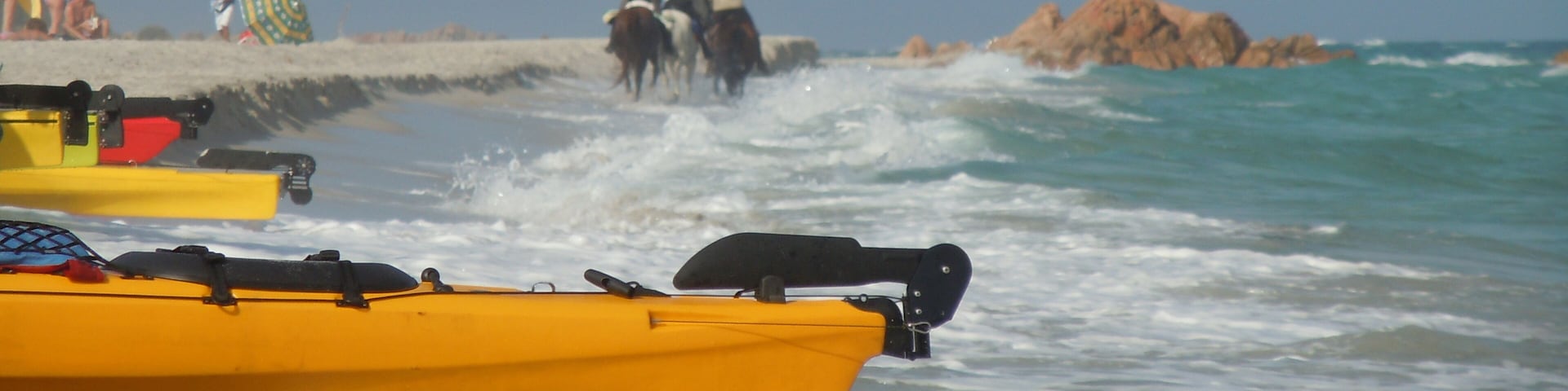 A beach with yellow kayaks, people in the water, and a rocky outcrop in the distance.
