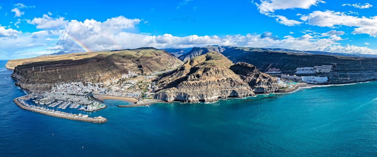 A coastal town with a prominent mountain, a marina, and a clear blue sky.