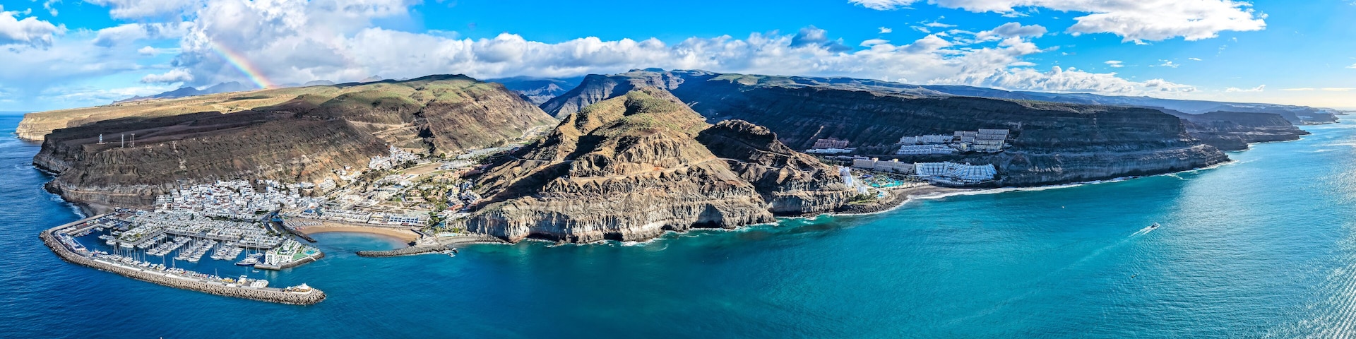 A coastal town with a prominent mountain, a marina, and a clear blue sky.