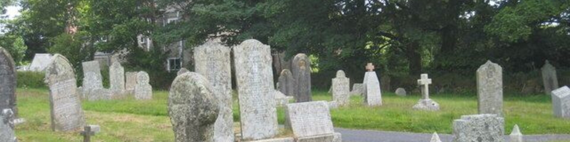 Um cemitério com numerosas lápides e cruzes, cercado por árvores e uma estrada.