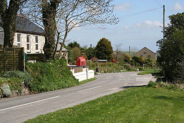 A rural road with houses, a red post box, and a stone building in the distance.