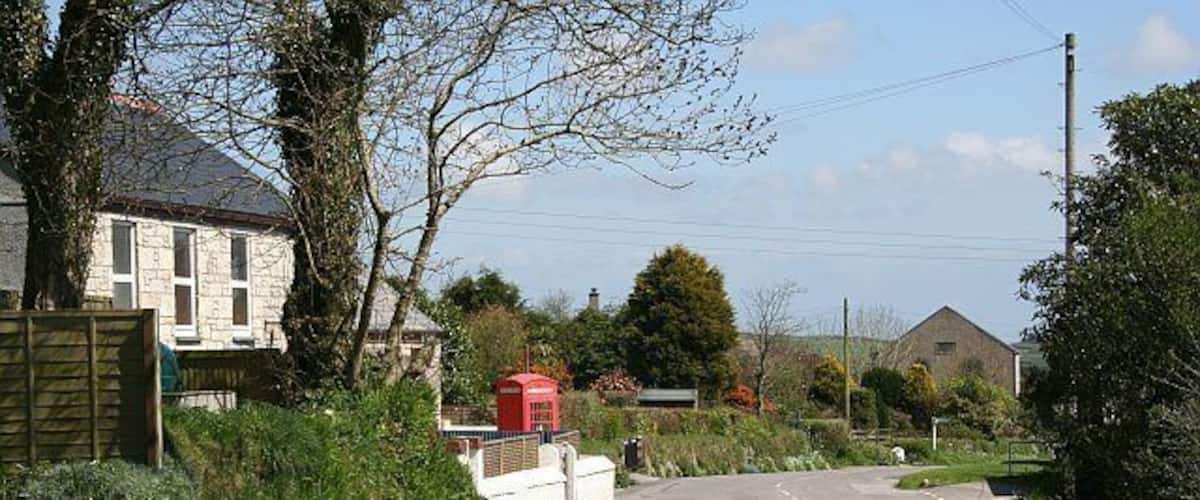 A rural road with houses, a red post box, and a stone building in the distance.