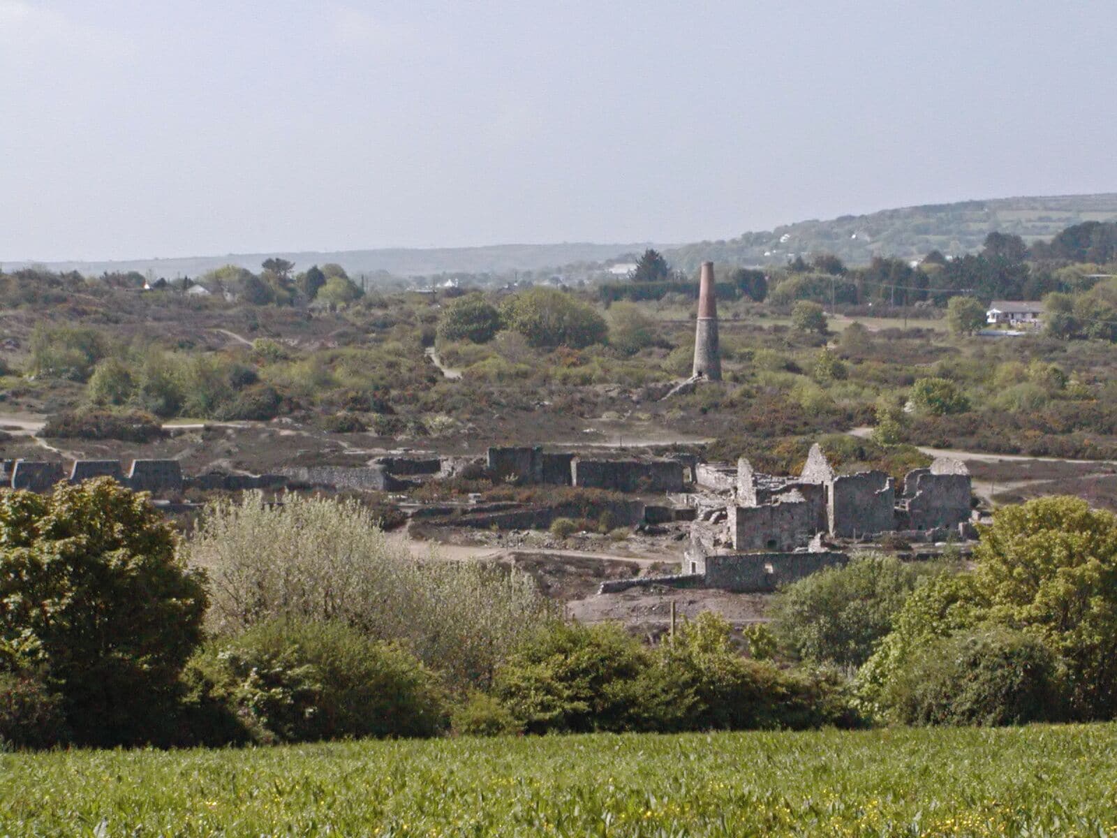 A rural landscape with a prominent red chimney, scattered ruins, and a field in the foreground.