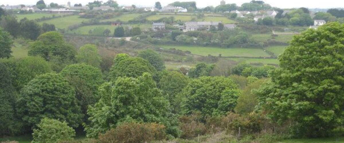 A rural landscape with rolling hills, scattered trees, and a few buildings in the distance.