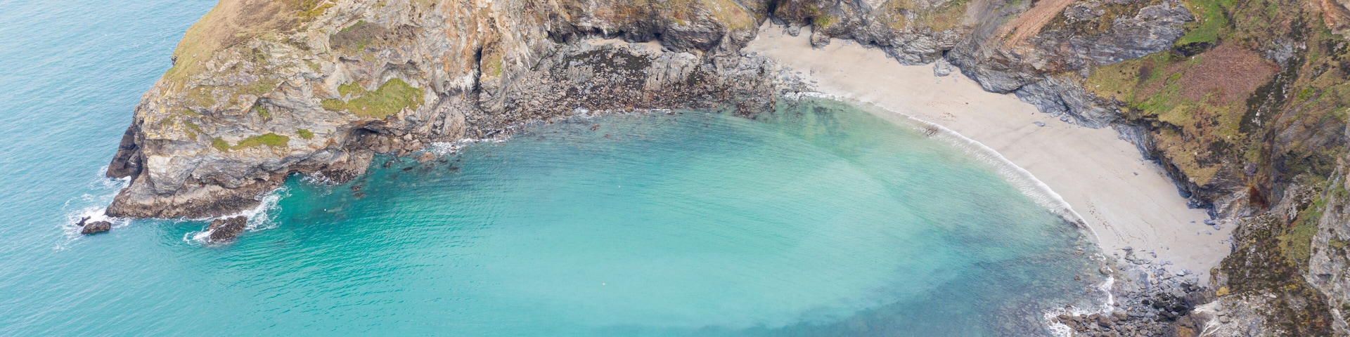 Un acantilado costero con playa, aguas turquesas cristalinas y campos de cultivo.