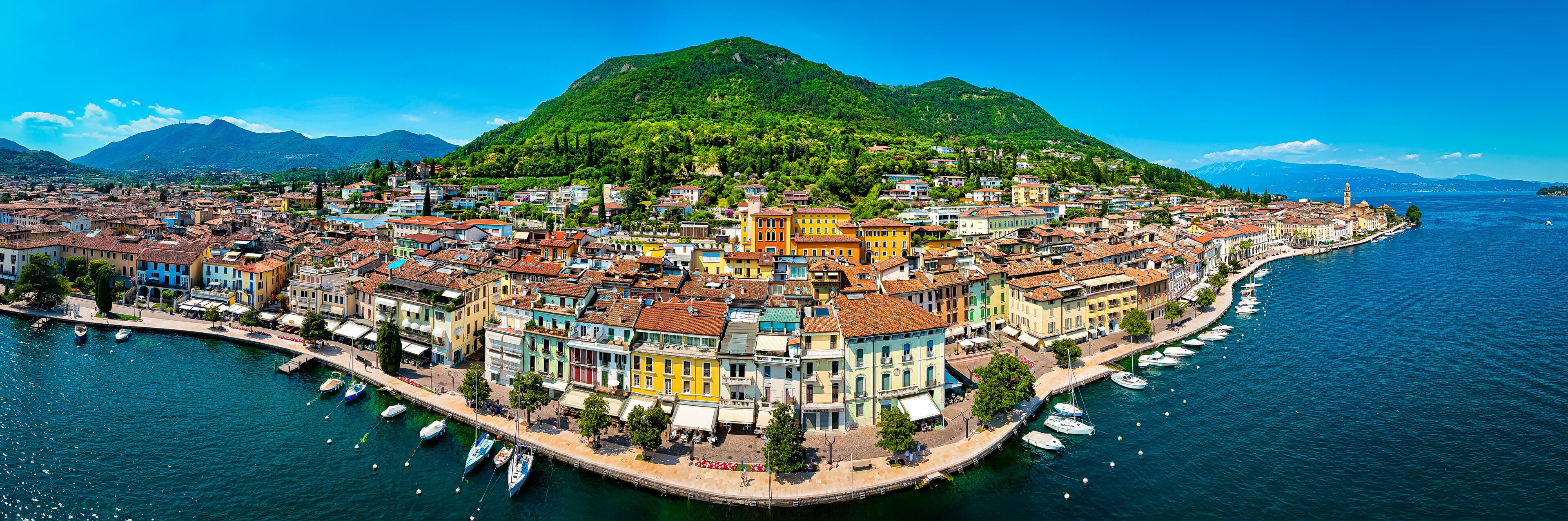 Aerial view of Salo, Italy with terracotta rooftops, lakeside promenade, and boats docked on the shore of Lake Garda on a sunny summer day