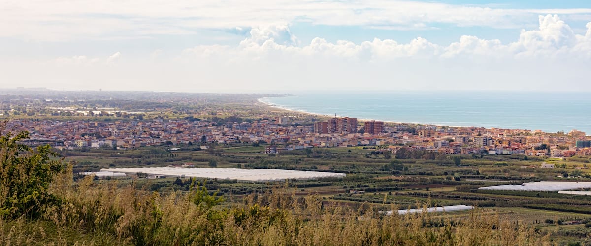 A coastal cityscape with a beach, green fields, and scattered buildings.