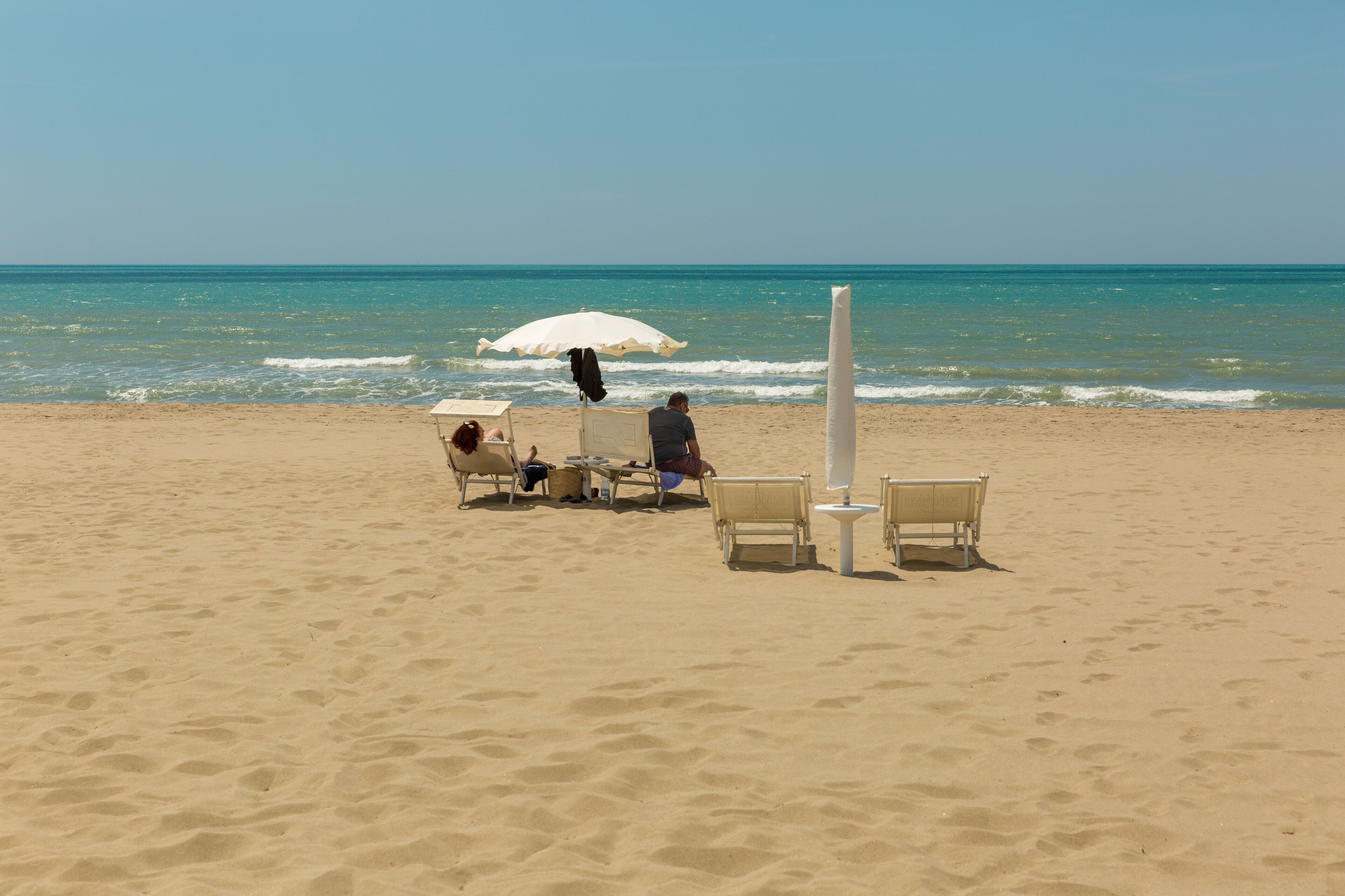 Una playa arenosa con algunas sillas y un paraguas blanco.
