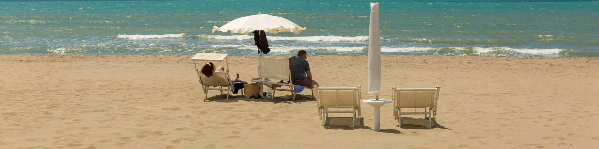Una playa arenosa con algunas sillas y un paraguas blanco.