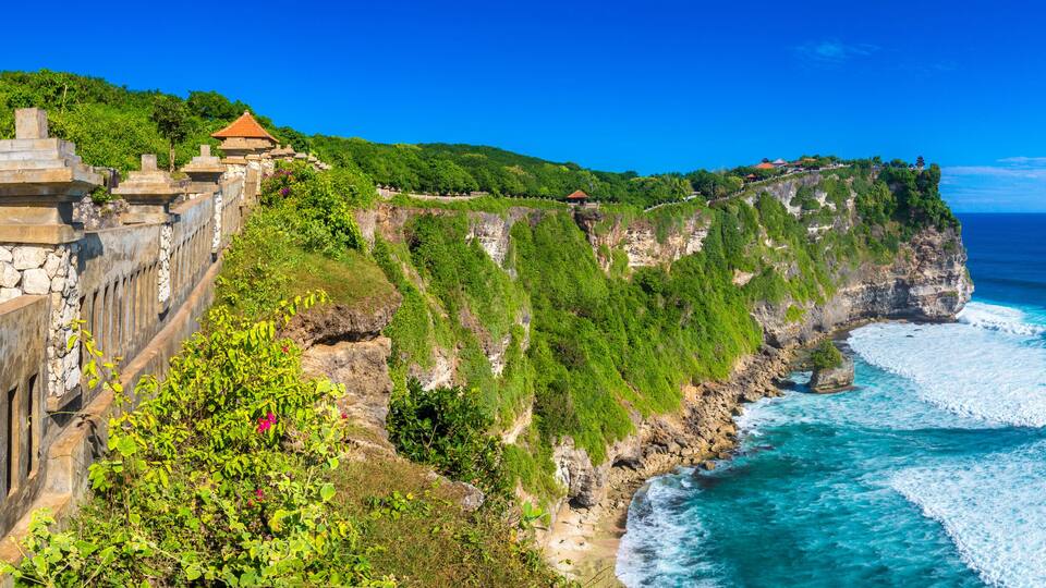 A coastal cliff with a stone wall and traditional buildings.