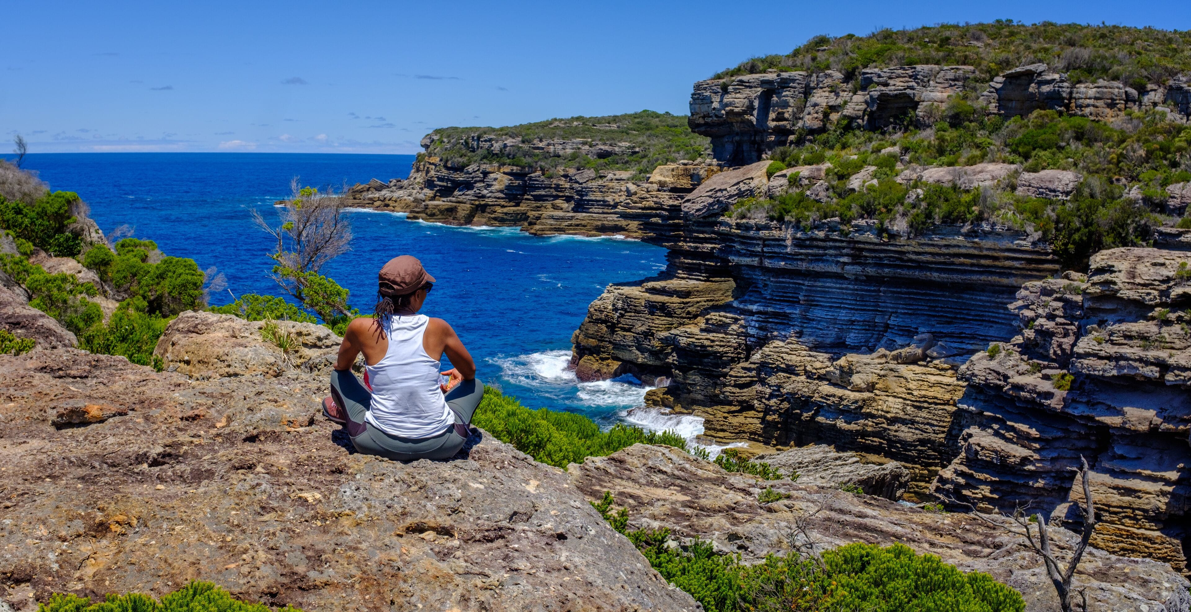 African Australian woman enjoying the dramatic coastal sea view and cliffs at Mermaids inlet, Beecroft Head, Abrahams Bosom Reserve, Jervis Bay, NSW, Australia