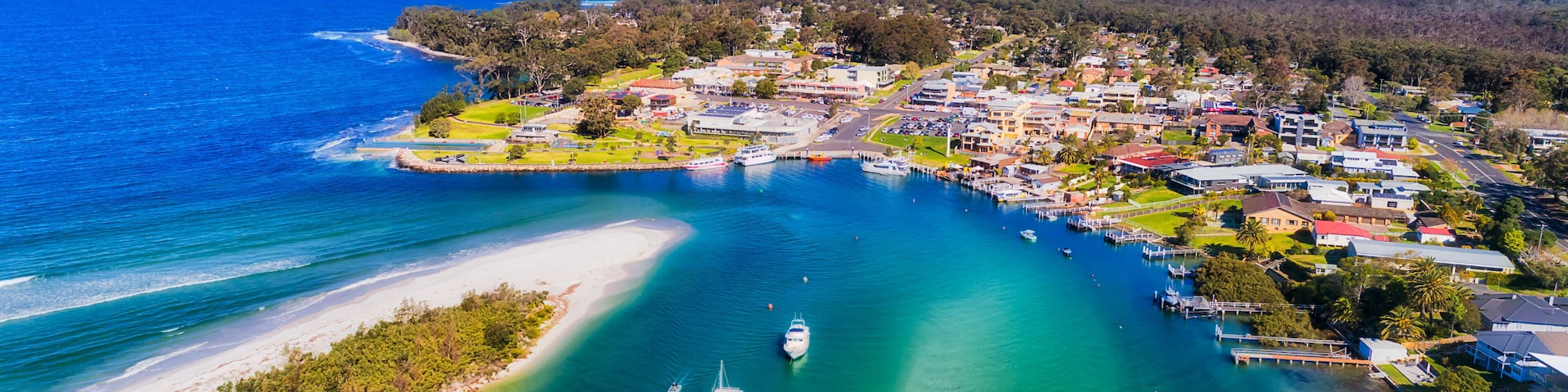 A coastal town with a marina, clear turquoise waters, and a sandy beach.