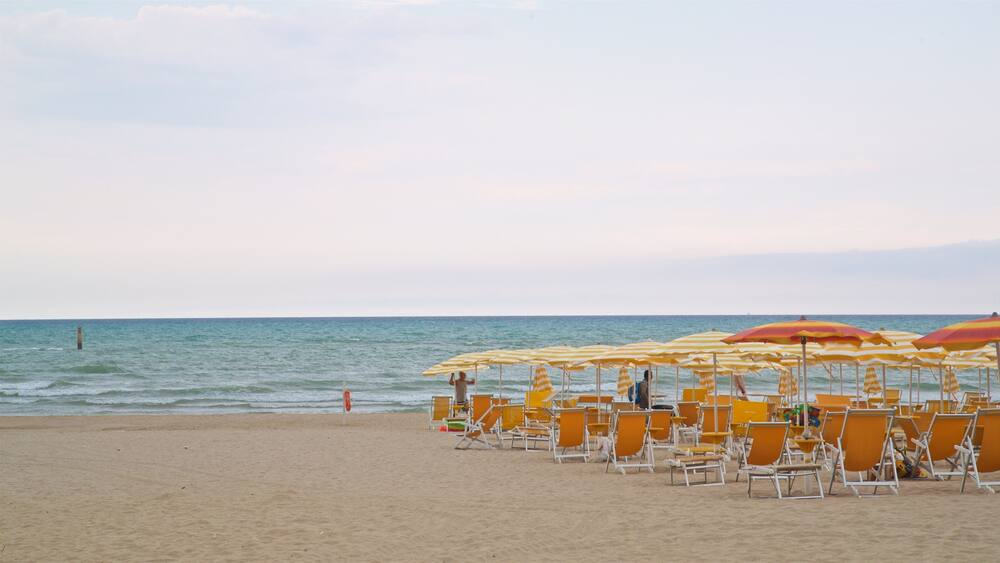 A beach with rows of yellow and red striped beach umbrellas and orange lounge chairs.