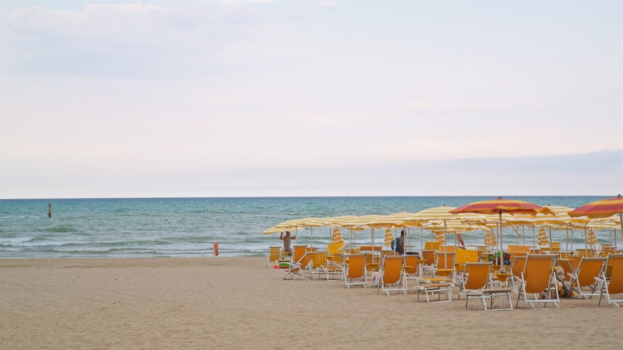 A beach with rows of yellow and red striped beach umbrellas and orange lounge chairs.