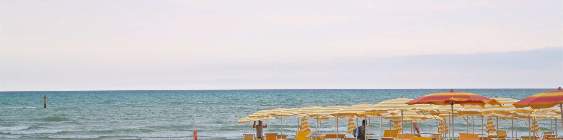 Una playa con hileras de sombrillas de playa amarillas y rojas, y sillones de descanso naranja.