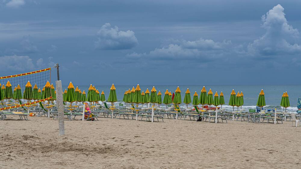 A beach with rows of green and yellow umbrellas, a volleyball net, and a sandy shore.
