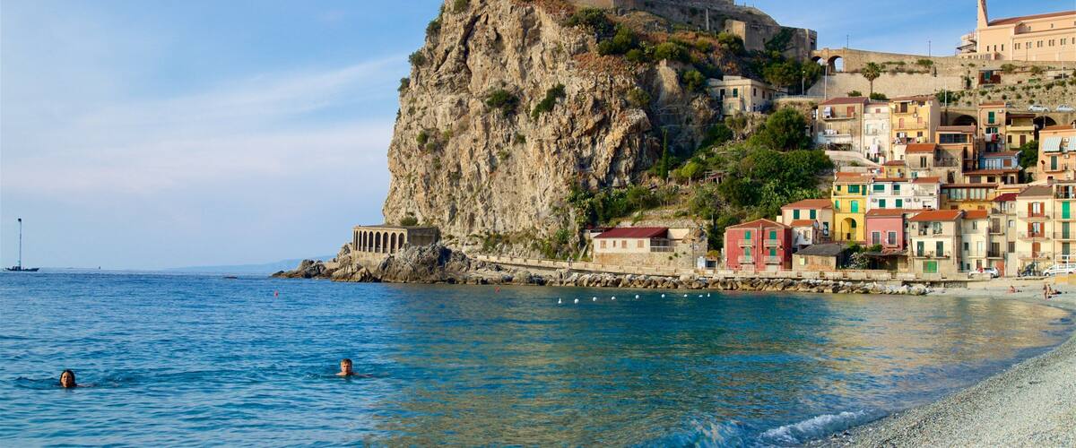 A coastal town with colorful buildings, a prominent cliff, and a castle on top.