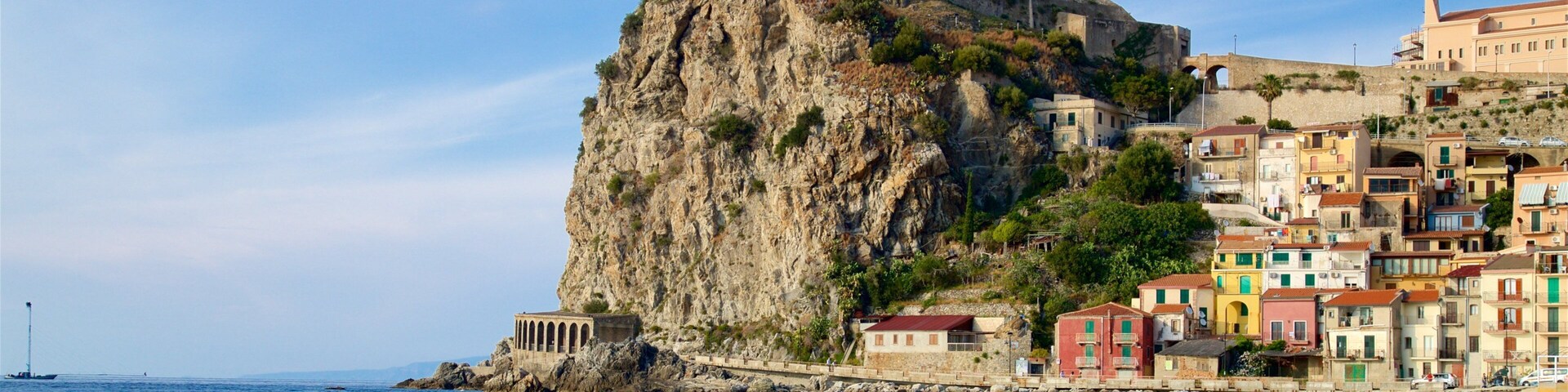 Uma cidade costeira com edifícios coloridos, um penhasco imponente e um castelo no topo.