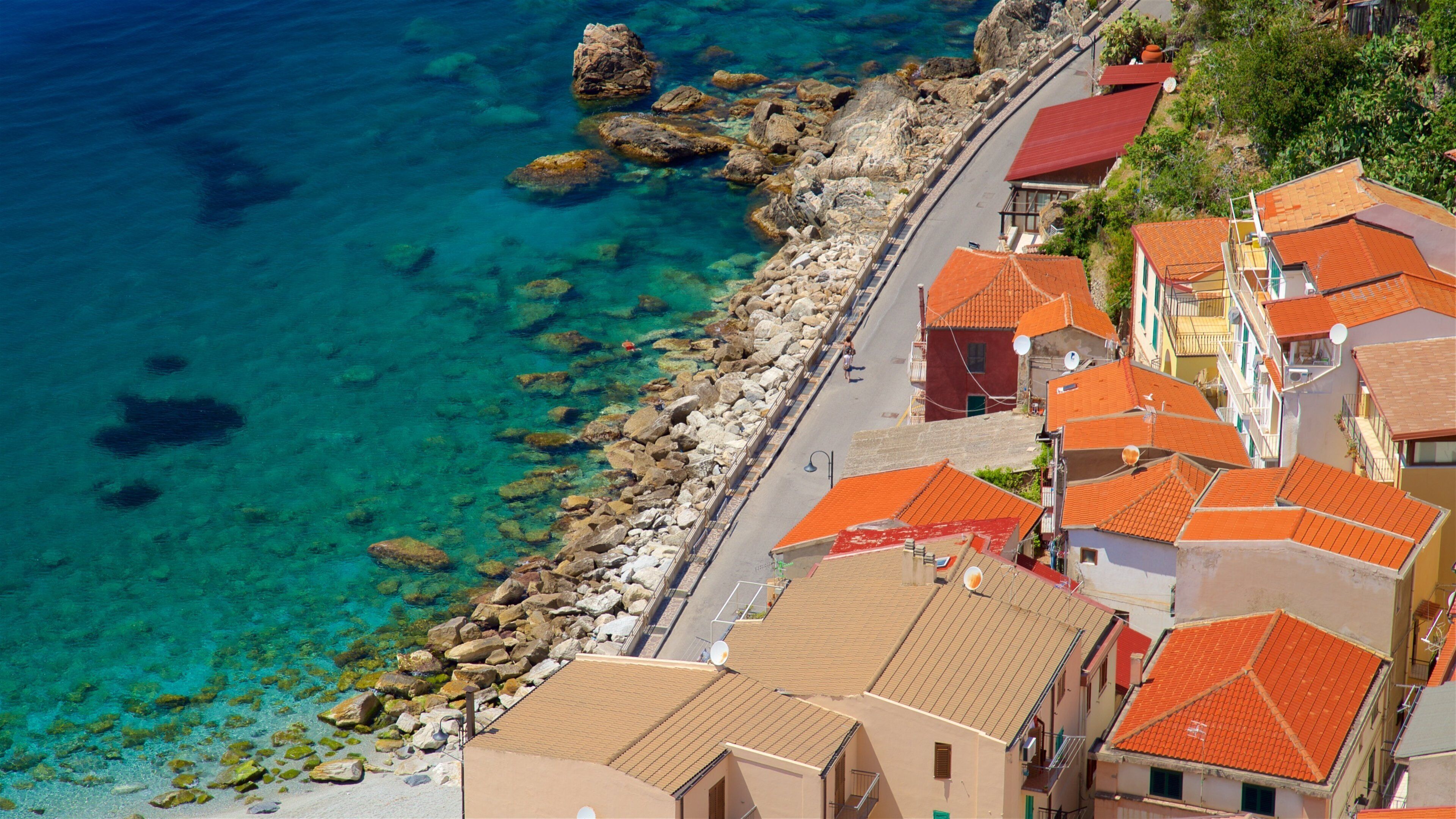 A coastal town with clear turquoise waters, rocky shoreline, and terracotta-roofed buildings.