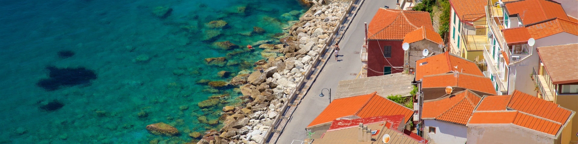 A coastal town with clear turquoise waters, rocky shoreline, and terracotta-roofed buildings.