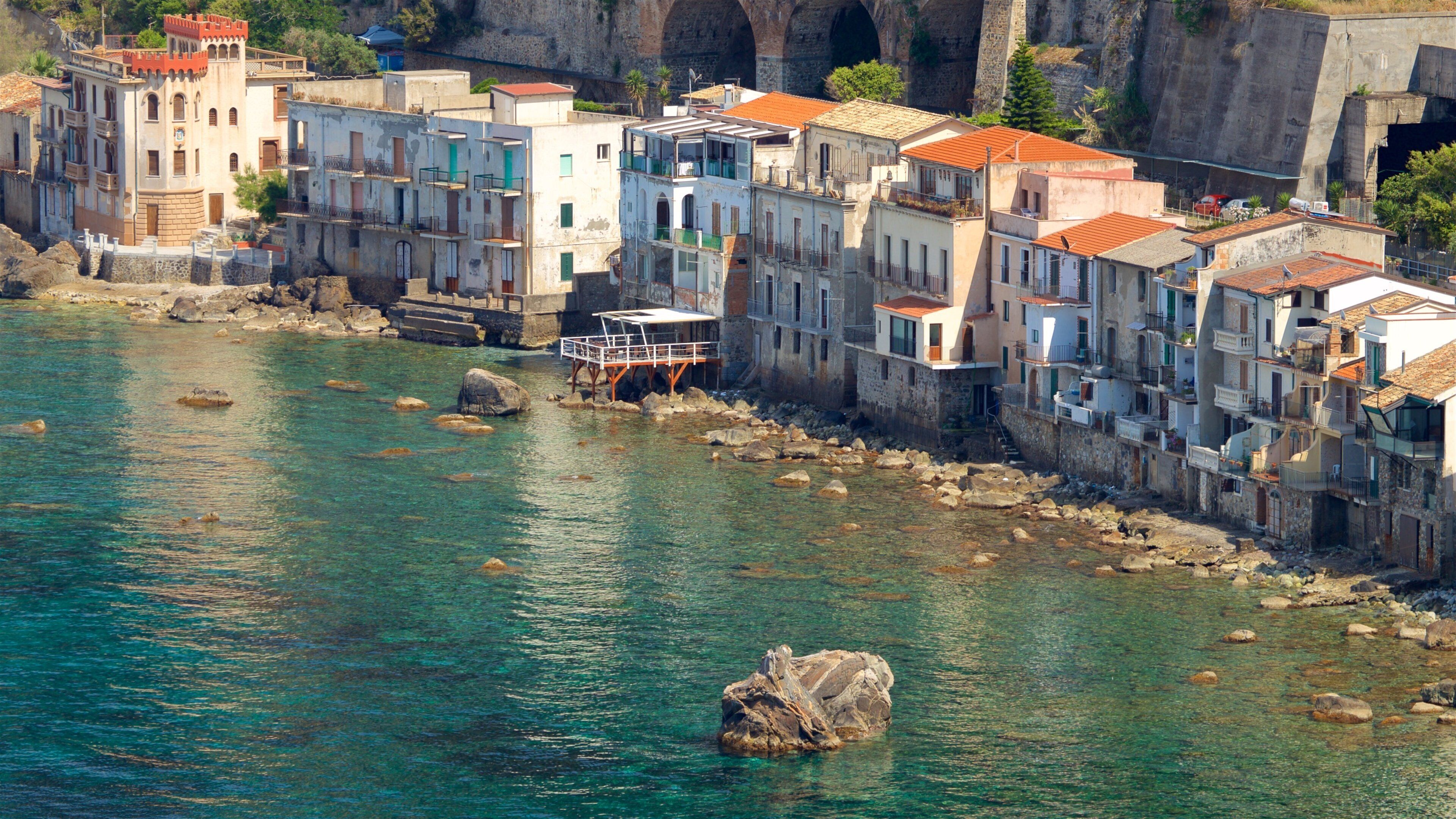 A coastal town with colorful buildings, a rocky shoreline, and clear turquoise water.
