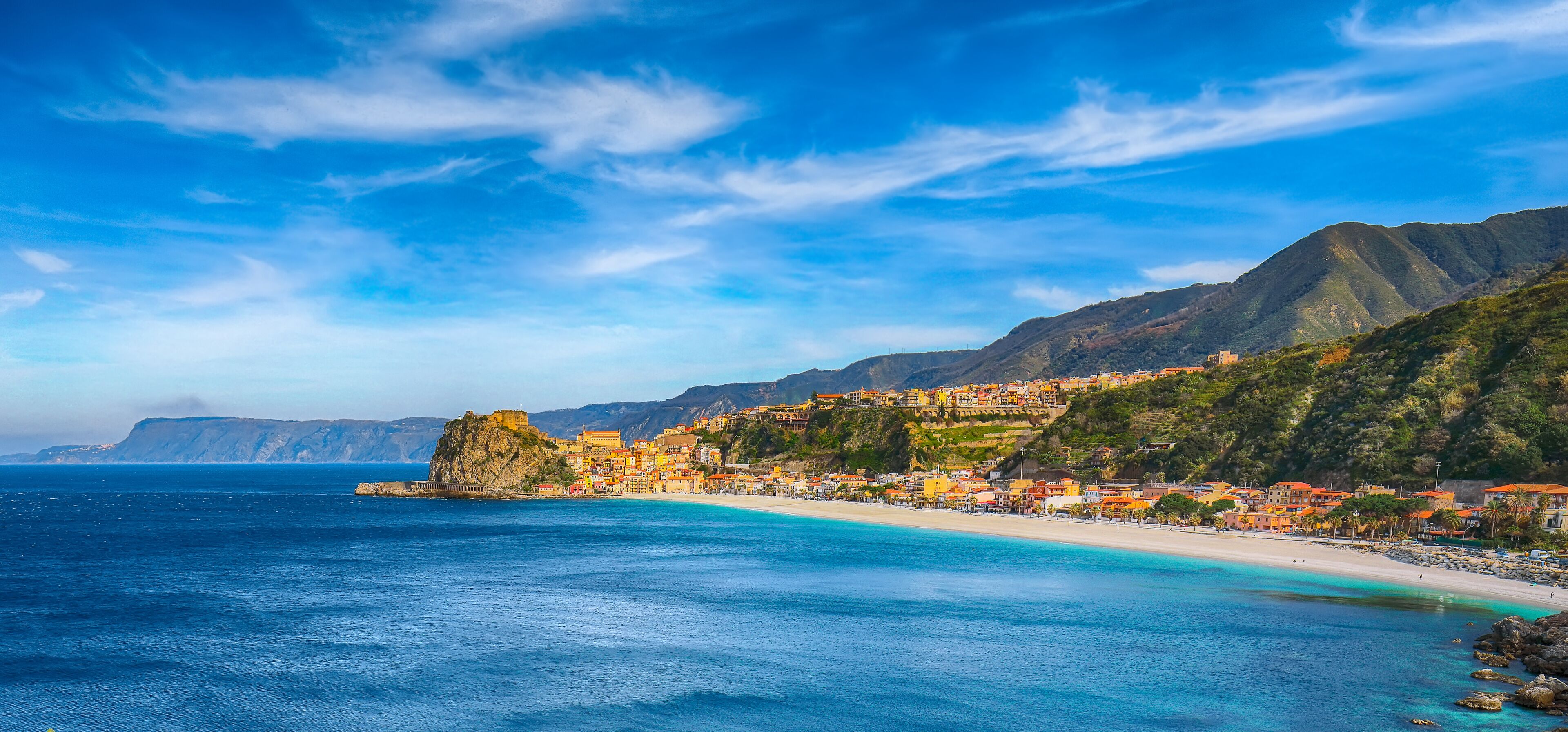 Un pueblo costero con edificios de colores, una playa y montañas al fondo.