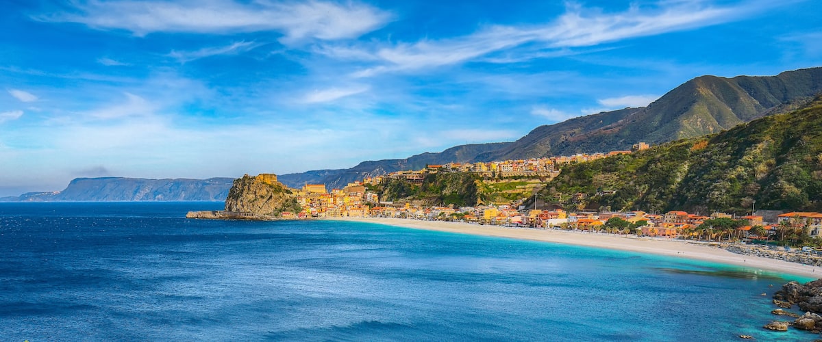 Un pueblo costero con edificios de colores, una playa y montañas al fondo.