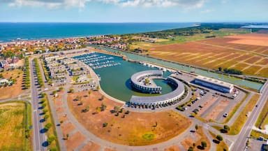 An aerial view of a coastal town with a marina, a large circular building, and surrounding fields.