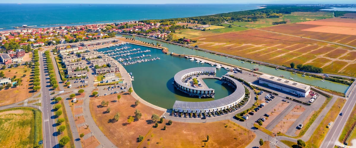 An aerial view of a coastal town with a marina, a large circular building, and surrounding fields.