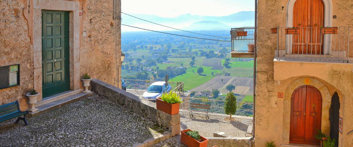 A cobblestone street with stone buildings, a green door, and a view of a valley.