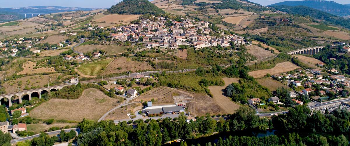 A town nestled in a valley with a prominent hill, vineyards, and a bridge.